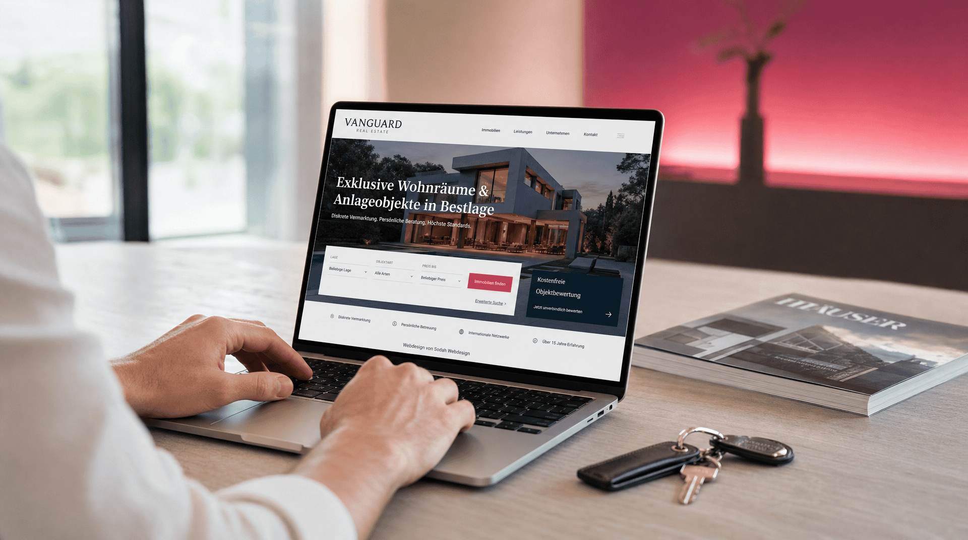 Person nutzt Laptop mit Immobilienmakler-Website zur Objektsuche und -bewertung. Schlüssel und Magazin liegen daneben.