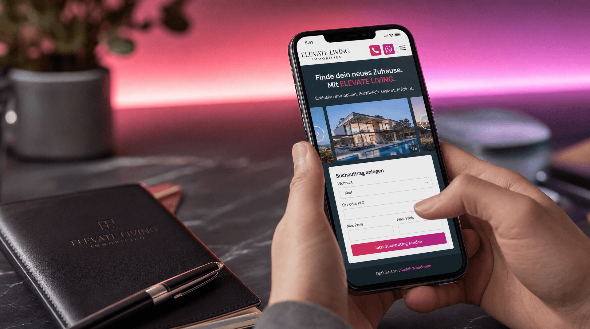 Hände halten Smartphone mit Immobilienmakler-Website, die ein Luxushaus und eine Objektsuche zeigt.