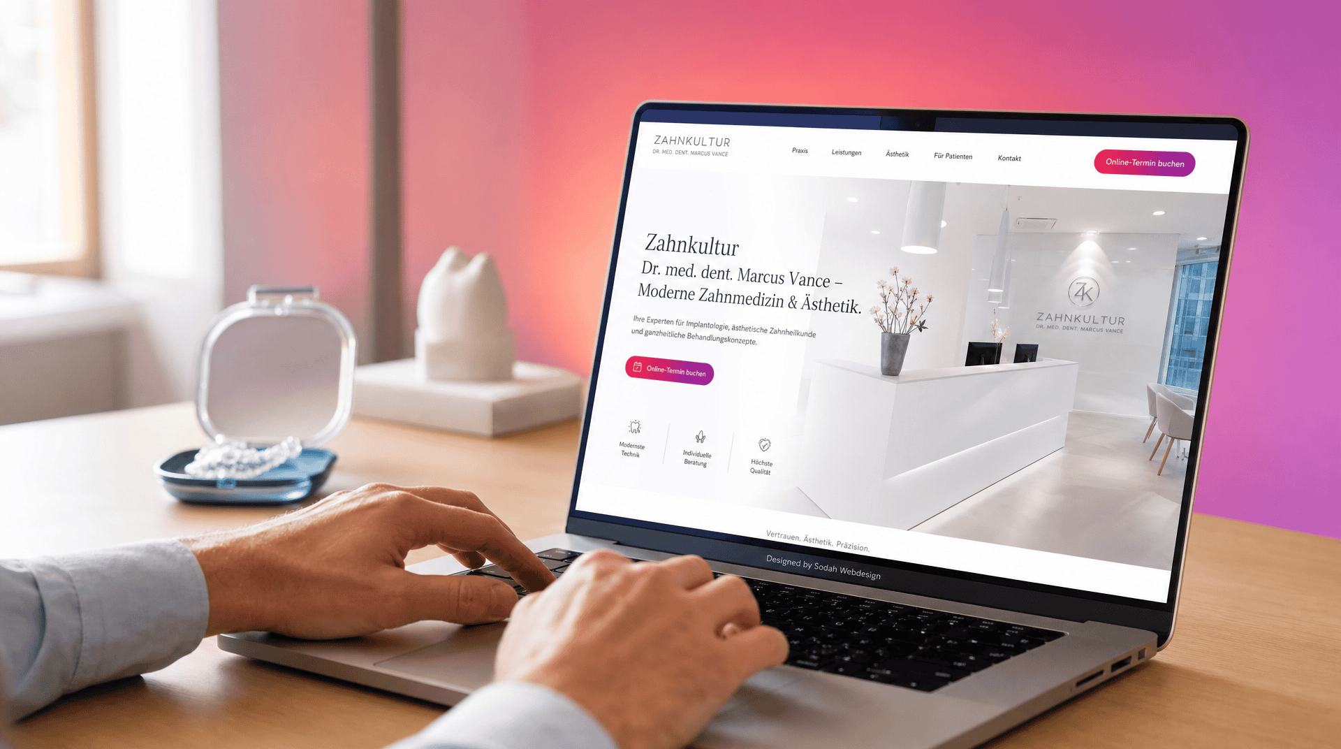 Nahaufnahme einer Person, die auf einem Laptop die Website einer Zahnarztpraxis mit Rezeptionsbereich und Online-Terminbuchung betrachtet, daneben ein Aligner-Behälter.